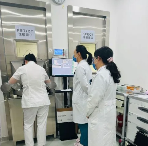 Hospital photograph of staff at PET/CT and SPECT preparation windows, an imaging workflow rather than a patient eligibility promise